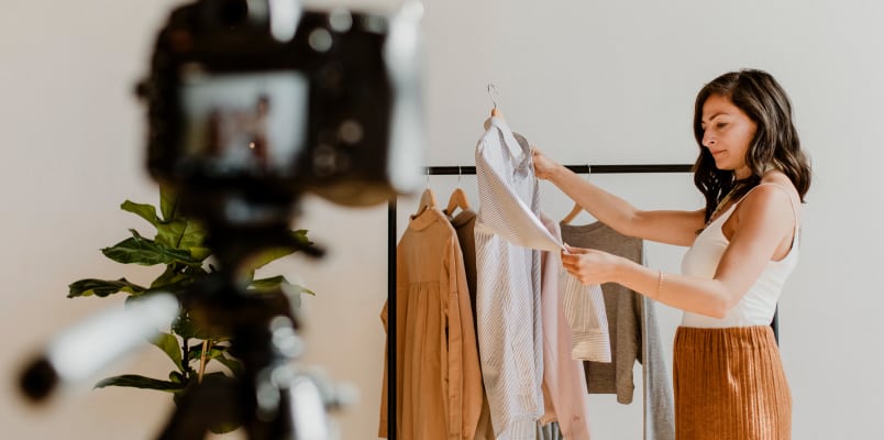 女性内容创造者,手里拿着一件衬衫站在相机前机架的衣服。