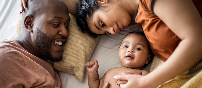 一个微笑的男人和女人躺在床上，他们微笑的婴儿夹在他们之间。