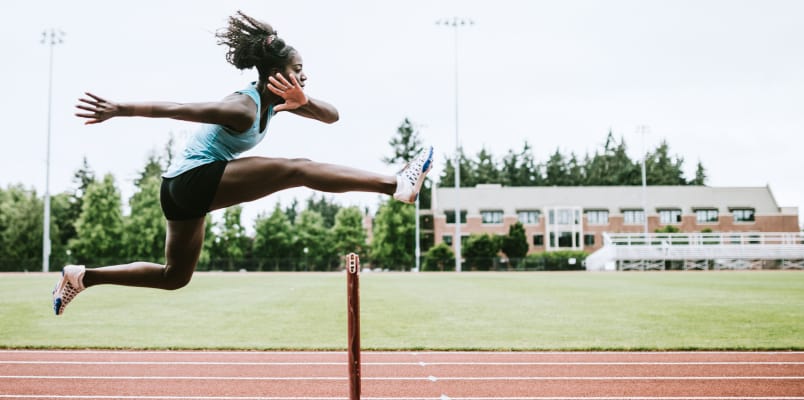 A female athlete jumping over hurdle on a sports track