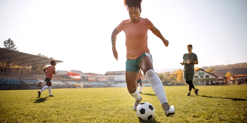 A woman in an orange shirt maneuvers a soccer ball.