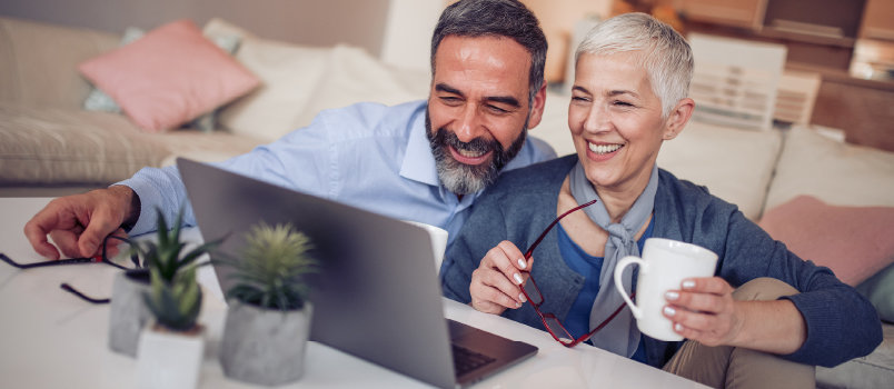 一个微笑的男人和一个女人手里拿着咖啡杯，看着她的笔记本电脑