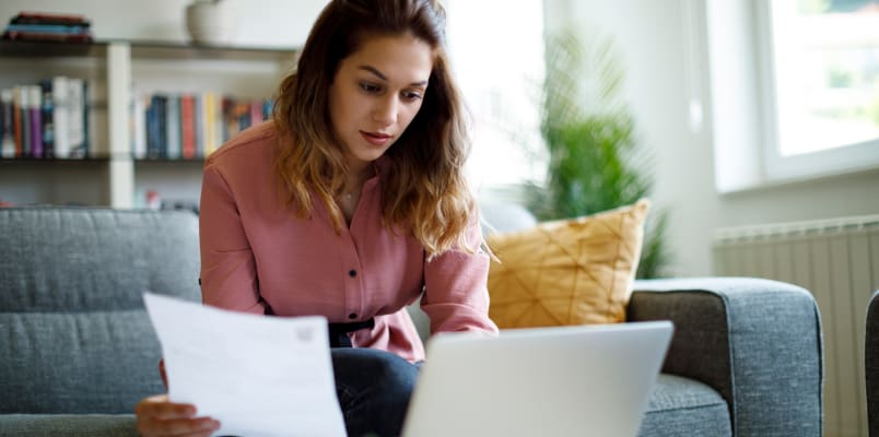 一名身穿粉色衬衫的女子一边查看1099-K税单，一边看着她的笔记本电脑。