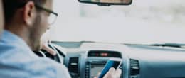 一个男人坐在他的车在使用TaxAct里程报销计算器在他的智能手机