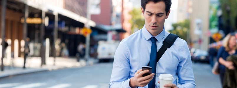 一个男人走在街上，一只手看手机，另一只手拿着咖啡